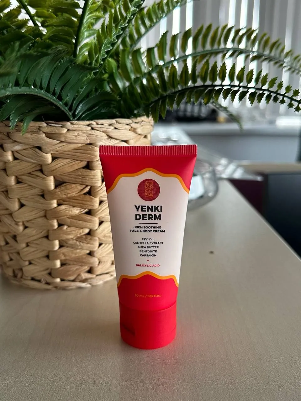 Tubo de Yenki Derm de 50 mL sobre un escritorio, delante de un helecho